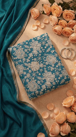 Blue embroidered fabric with white patterns on a beige surface with pink roses and petals.